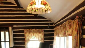 A dining area with a wooden table and chairs, a stained glass light fixture, and a television in the background. - "The Old Homestead"  An Original Homestead Cabin (Trout Creek)