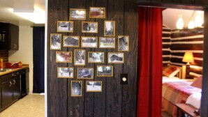 A room with a wooden wall adorned with framed photographs, a red curtain, and a bed with a striped blanket. - "The Old Homestead"  An Original Homestead Cabin (Trout Creek)