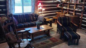 A cozy log cabin-style living room with a sofa, chairs, a coffee table, and a bookshelf. - "The Old Homestead"  An Original Homestead Cabin (Trout Creek)