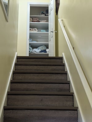 A staircase leading to a storage closet with shelves containing folded towels and linens. - Close to Beaches to Relax and Refresh (Swansboro)
