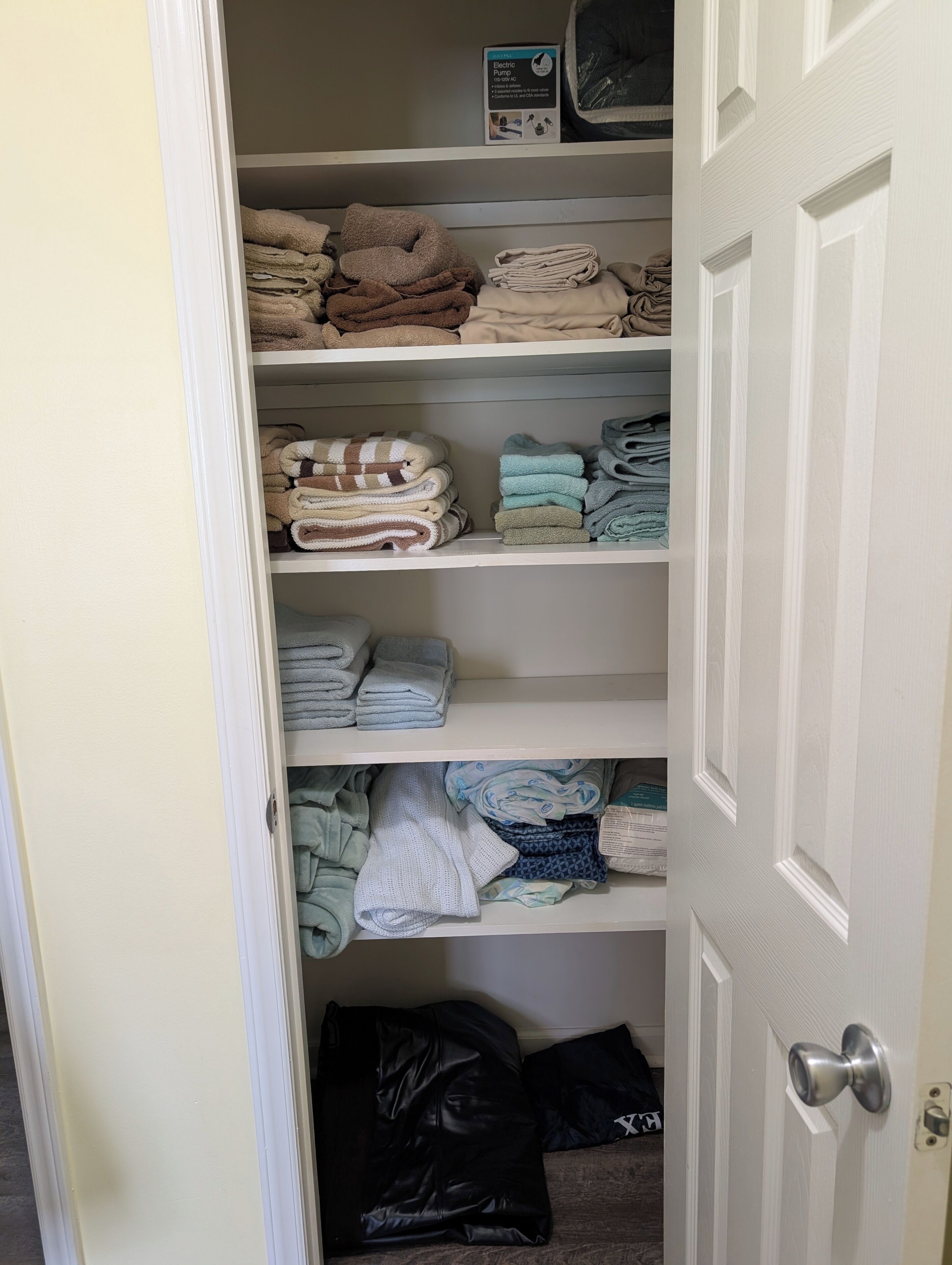 A closet with shelves containing folded towels and a black bag on the floor.