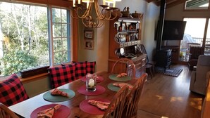 Un comedor con mesa de madera, cojines de cuadros rojos y negros, y una araña.