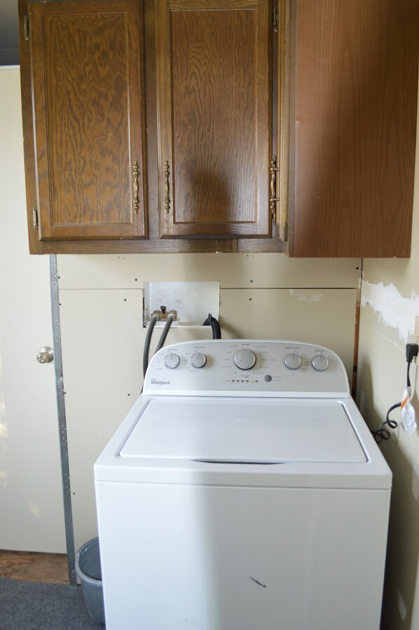 A white Whirlpool washer in a kitchen with wooden cabinets and a visible plumbing setup.