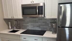 A kitchen with white cabinets, a stainless steel microwave, a refrigerator, a black stovetop, and a patterned tile floor.