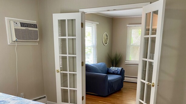 A bedroom with a bed, a bench, and an open door leading to another room.