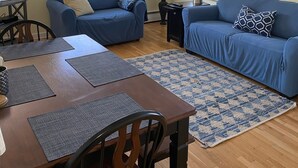 A living room with two blue sofas, a dining table with placemats, a TV, and a painting on the wall.