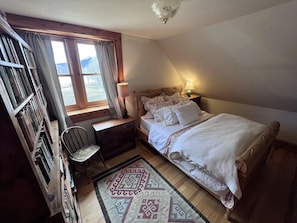 Une chambre à coucher comprenant un lit, un bureau, une chaise, une fenêtre avec des rideaux et un tapis à motifs.