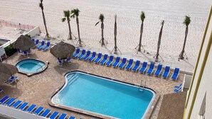 A pool area with blue lounge chairs, a large rectangular pool, and palm trees. - Beautiful Beach! Spectacular Sunsets! (Redington Shores)