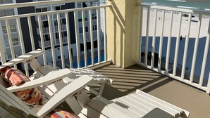 A balcony with white lounge chairs and colorful cushions, overlooking a beach and a building with balconies. - Beautiful Beach! Spectacular Sunsets! (Redington Shores)