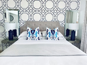 Quarto de hotel com uma cama grande, duas mesas de cabeceira, duas luminárias e um papel de parede estampado.