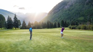 Campo de golf con montañas al fondo, que presenta un césped cuidado y árboles.