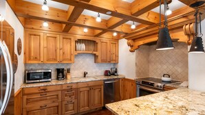 Una cocina con armarios de madera, encimeras de granito, electrodomésticos de acero inoxidable y lámparas colgantes.