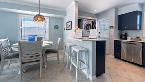 A modern kitchen with a built-in washer and dryer, a dining area with a table and chairs, and a hanging light fixture.