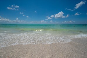 Ein Strand mit klarem türkisblauem Wasser, sanften Wellen und einigen badenden Personen.