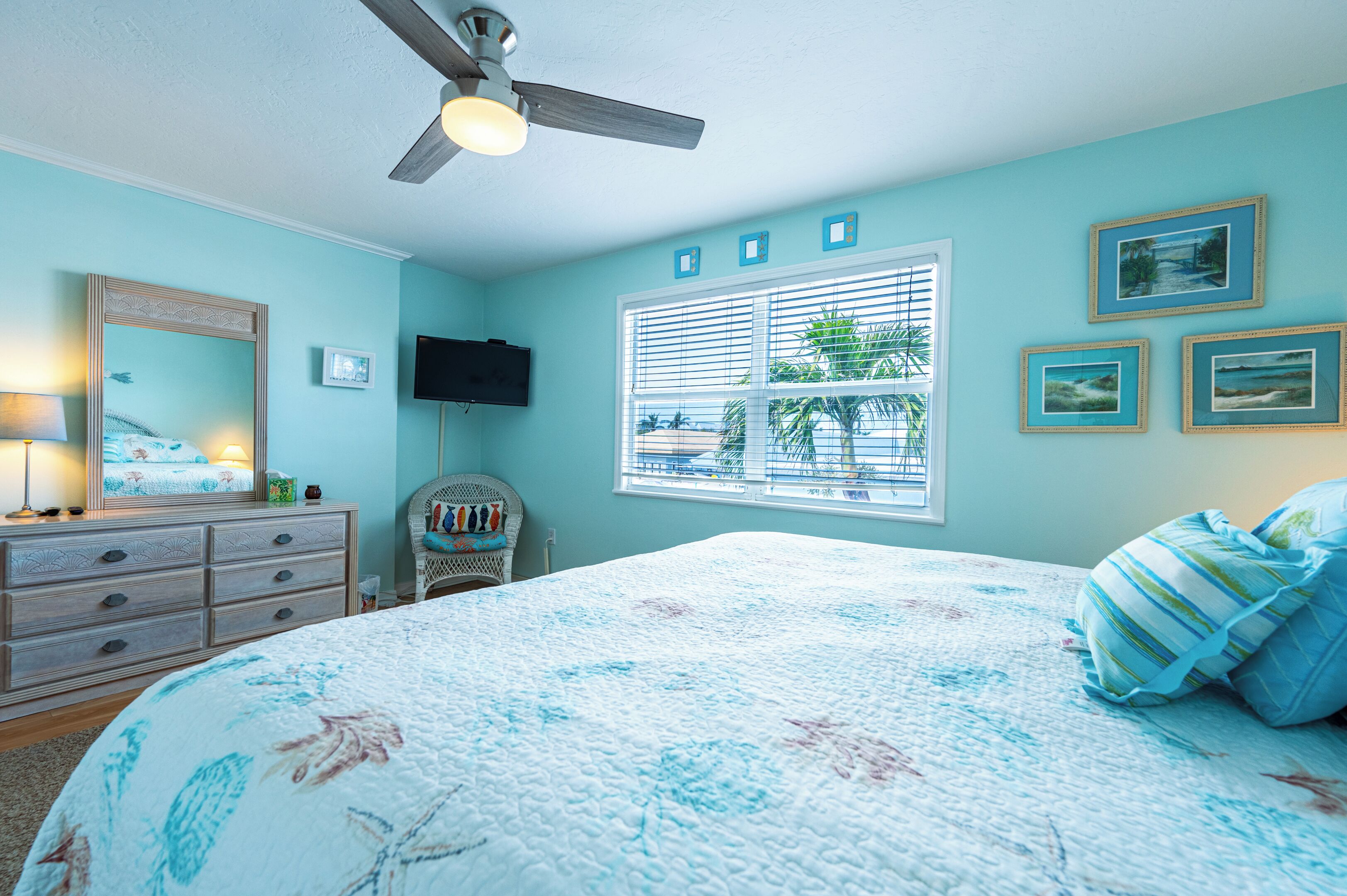 Une chambre à coucher comprenant un lit, une commode, un ventilateur de plafond et une fenêtre avec des stores.