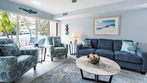 A living room with a blue sofa, matching armchairs, a coffee table, and a painting of a beach scene.