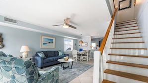 A living room with a blue sofa, a patterned armchair, a coffee table, and a ceiling fan.