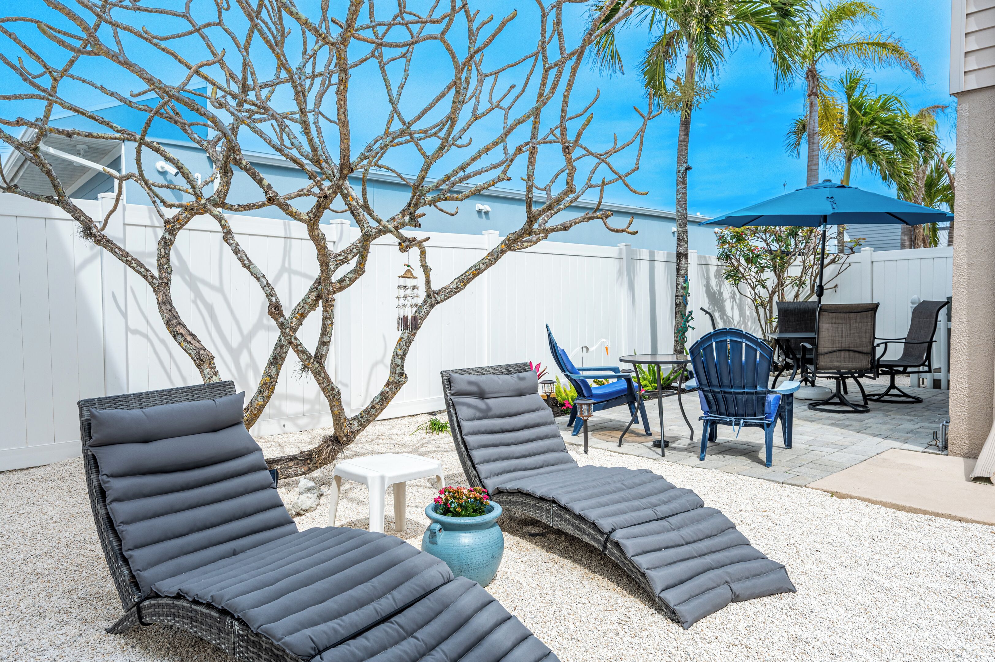 Um quintal com duas cadeiras de descanso, uma mesa pequena e um guarda-sol azul.