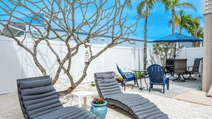A backyard with two lounge chairs, a small table, and a blue umbrella.