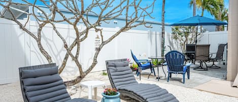A backyard with two lounge chairs, a small table, and a blue umbrella.