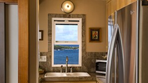 Una cocina con armarios de madera, un refrigerador de acero inoxidable, una ventana con vista al mar y una lámpara empotrada.