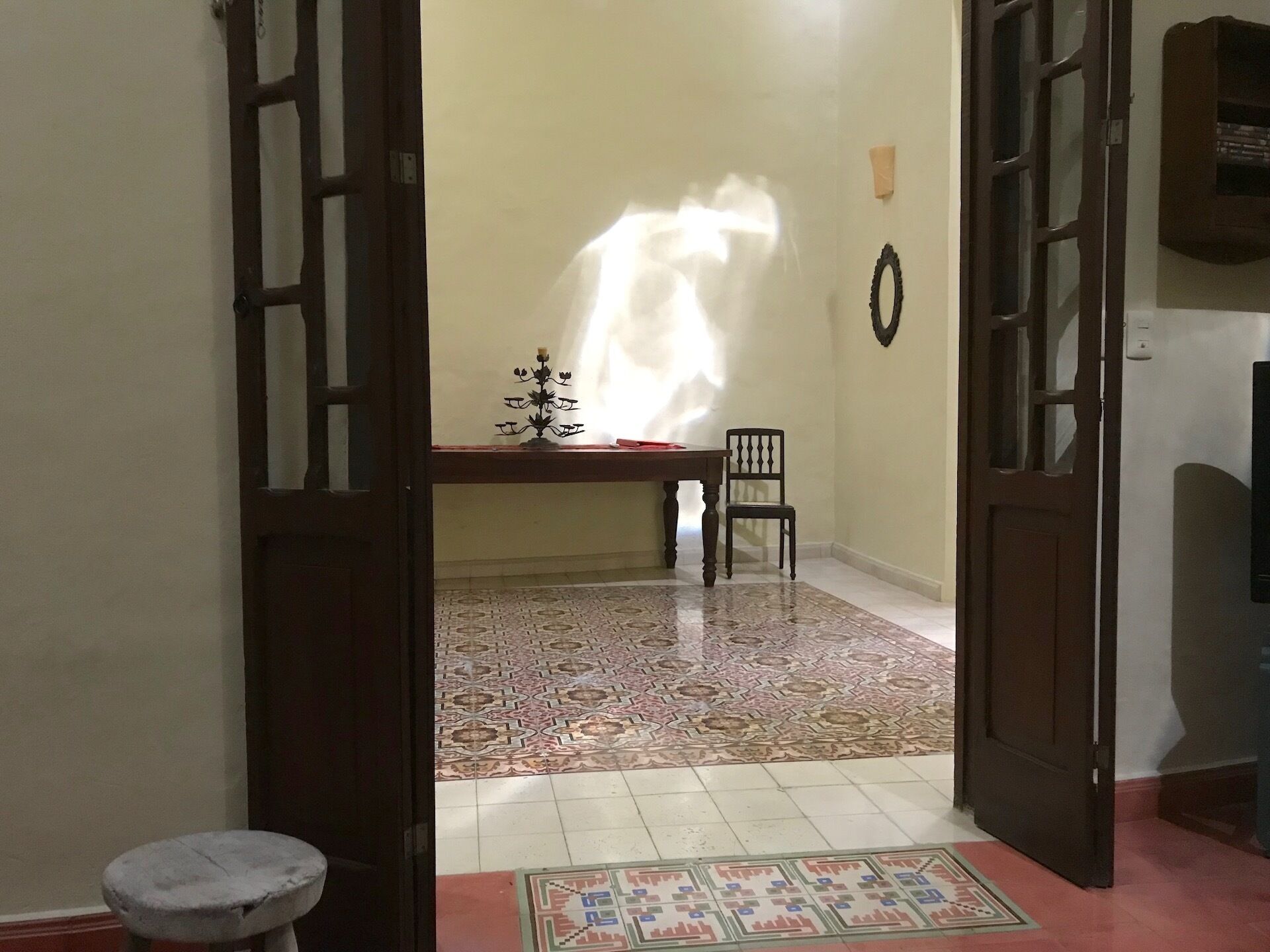 A room with a patterned floor, a table with a candelabra, a chair, and a door.