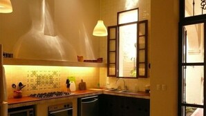 A compact kitchen with a gas stove, oven, and dishwasher. There is a window with a view of the outside, and a hanging light fixture above the counter.