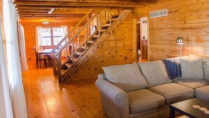 A wooden interior with a staircase, a sofa, and a dining area.