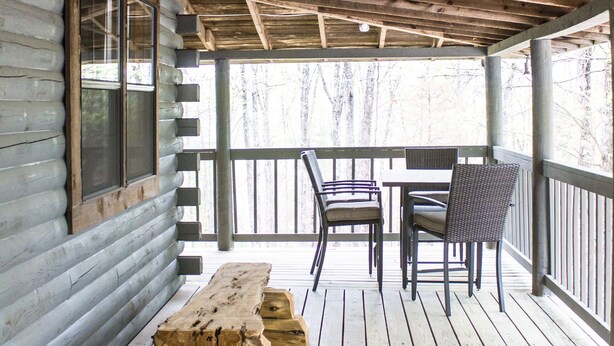 A wooden deck with a table and chairs, a window, and a view of trees.