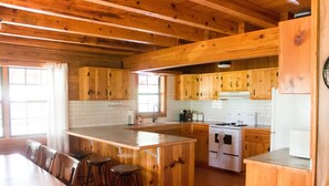 A wooden kitchen with a central island, bar stools, and a dining table.