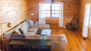 A cozy cabin interior with a wooden interior, a sofa set, a rocking chair, and a small table.