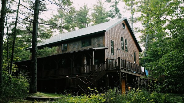A wooden cabin with a balcony, surrounded by trees. - Lake Superior Beachfront, 4+ Bedrooms, Spectacular Timberframe Home (Washburn)