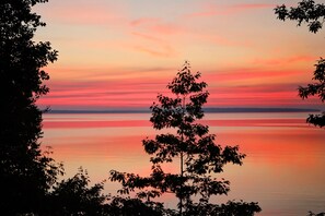 A serene lake at sunset with a tree in the foreground. - Lake Superior Beachfront, 4+ Bedrooms, Spectacular Timberframe Home (Washburn)