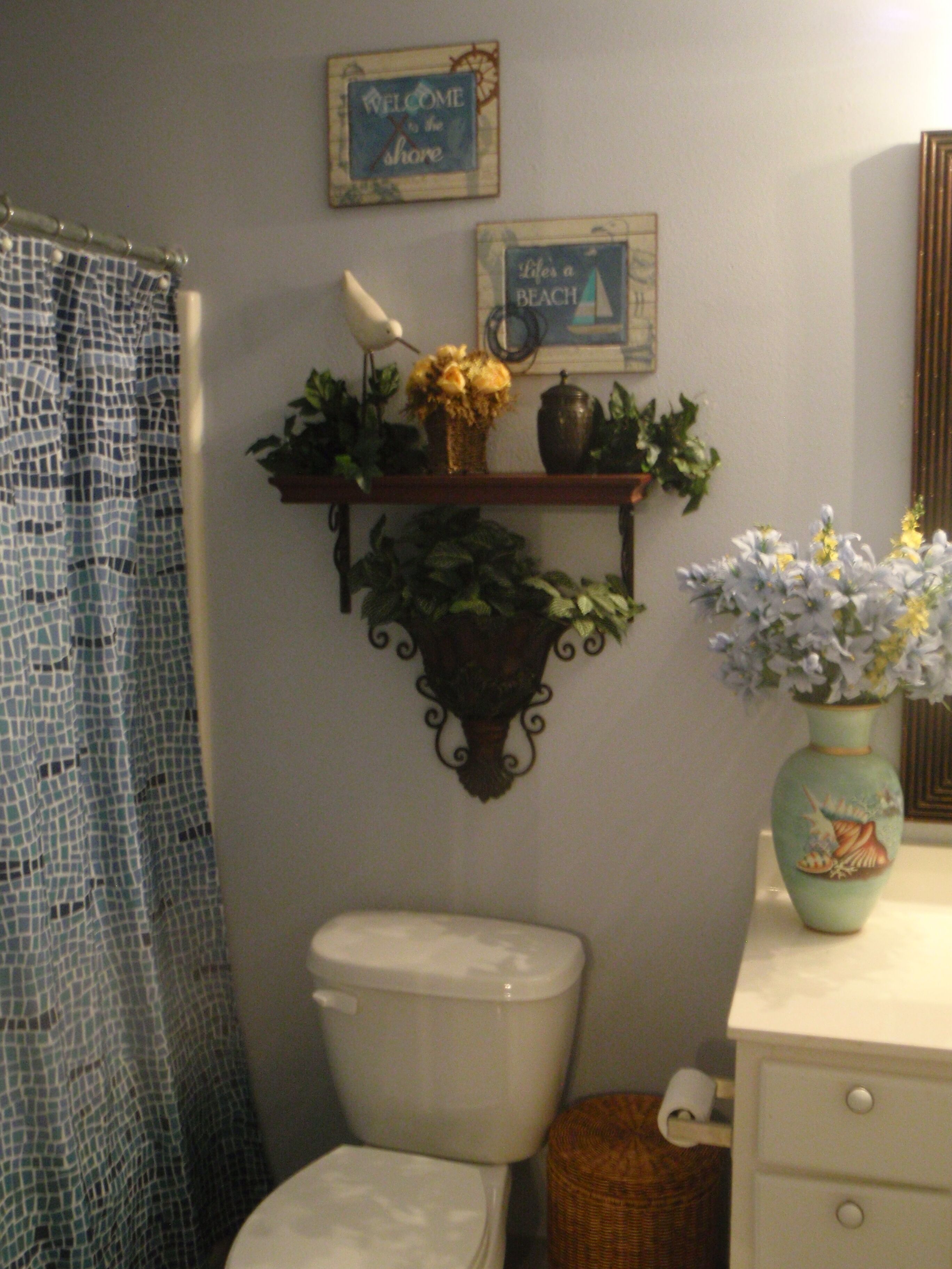 A bathroom with a toilet, a shelf with plants, a vase with flowers, and a shower curtain.