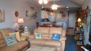 A living room with a beige sofa, a coffee table, and a dining area with a wooden table and chairs. - Family Owned Waterfront 3 Bedroom/2 Bath Fully Furnished Condo (Venice)