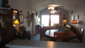 A spacious living area with a dining table, chairs, and a ceiling fan. There is a kitchen area with granite countertops and a sink. - Family Owned Waterfront 3 Bedroom/2 Bath Fully Furnished Condo (Venice)
