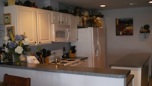 A kitchen with white cabinets, a microwave, a refrigerator, a stove, and two bar stools. - Family Owned Waterfront 3 Bedroom/2 Bath Fully Furnished Condo (Venice)