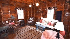 L’intérieur d’un chalet confortable, avec un canapé, deux fauteuils, un banc et une table sur laquelle se trouve une lampe.