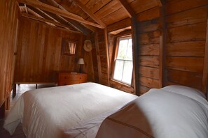 Ein Schlafzimmer einer Holzhütte mit Bett, Schminktisch und Fenster.