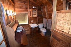 Ein Badezimmer in einer Holzhütte mit Waschbecken, Toilette und einer Sitzbank mit Handtüchern.