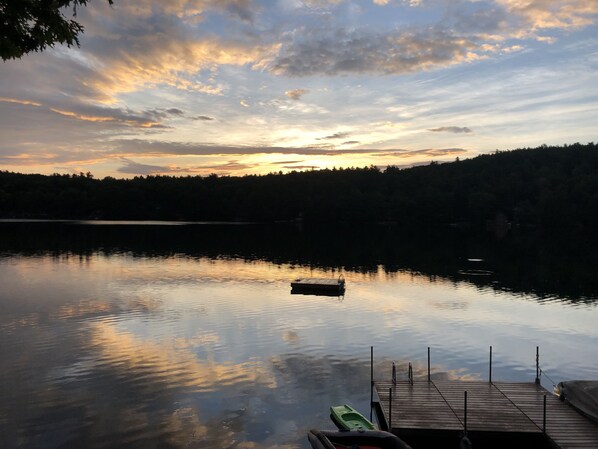 Ein stiller See bei Sonnenuntergang mit einem Steg und einem kleinen Boot.