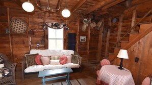 L’intérieur d’un chalet confortable, avec une cheminée, un canapé, une table recouverte d’une nappe à carreaux et une tête de cerf accrochée au mur.
