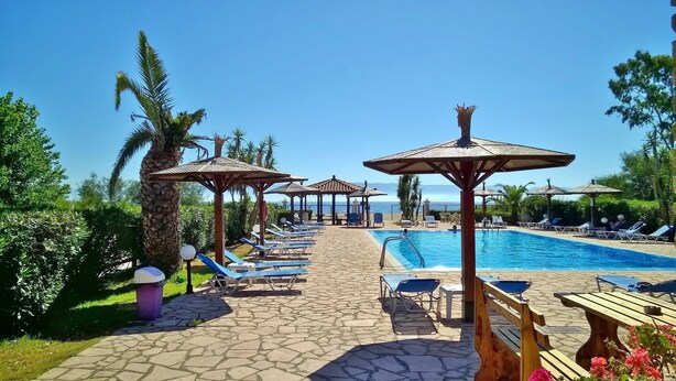 A poolside area with lounge chairs, umbrellas, and a clear view of the sea.