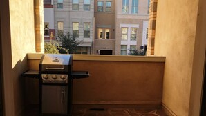 A balcony with a grill, stone flooring, and a view of neighboring buildings.