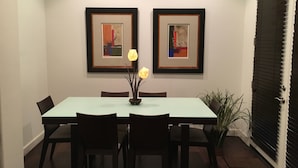 A dining area with a rectangular table, four chairs, two framed artworks on the wall, and a potted plant.