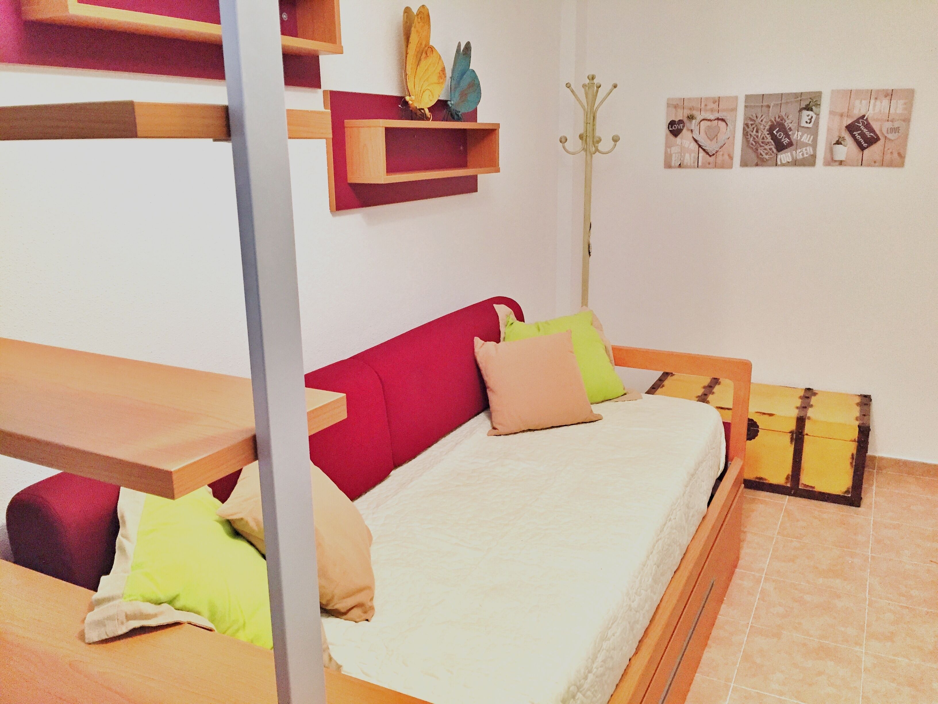 A bedroom with a bed, a red headboard, and a wooden bench. There are pillows on the bed and a coat rack against the wall.