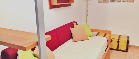 A bedroom with a bed, a red headboard, and a wooden bench. There are pillows on the bed and a coat rack against the wall.