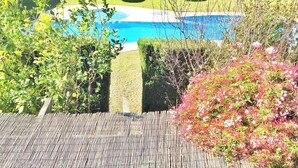 Zona de piscina con cerramiento de bambú, setos y vista a una piscina.