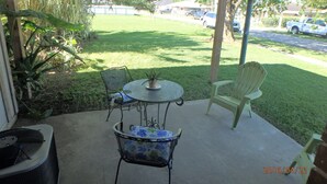 A patio with a round table and chairs, a potted plant, and a trash can.