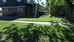 A two-story brick house with a covered porch, a lawn, and a large tree.